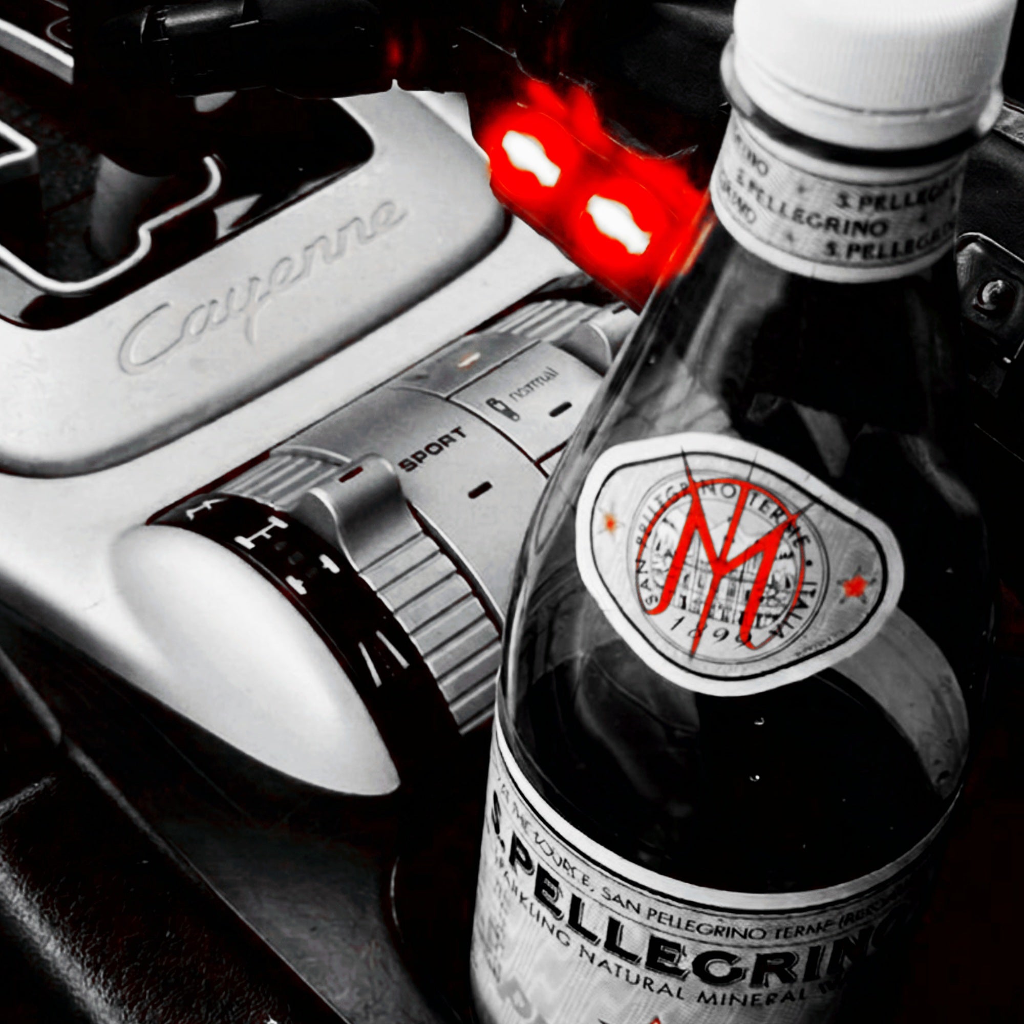 A bottle of San Pellegrino Mineral Water in the 'Pellegrino' variant, styled in a Porsche Cayenne center console next to a silver gear shift knob and a black gear selector, with a selective color effect leaving the bottle and console in sharp focus.

The Mars23arth symbol shines in red.