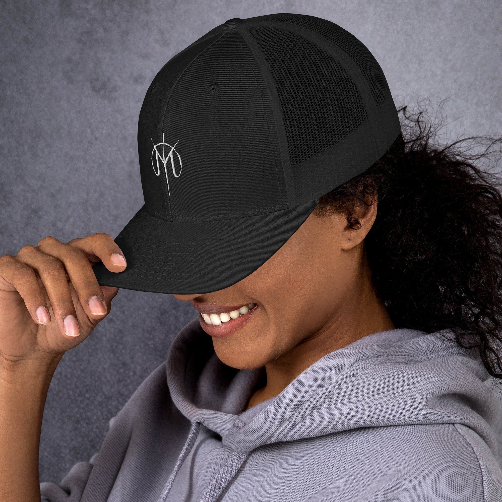 Person wearing a black cap with a small embroidered design, Letters from mars M logo smiling against a gray background