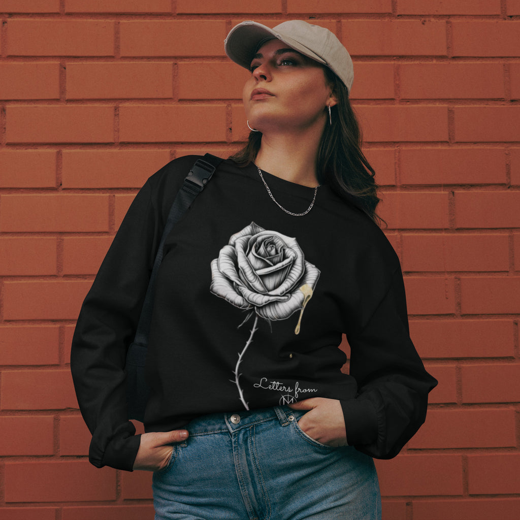 Person wearing a black sweatshirt with a Letters from Mars rose design against a brick wall.