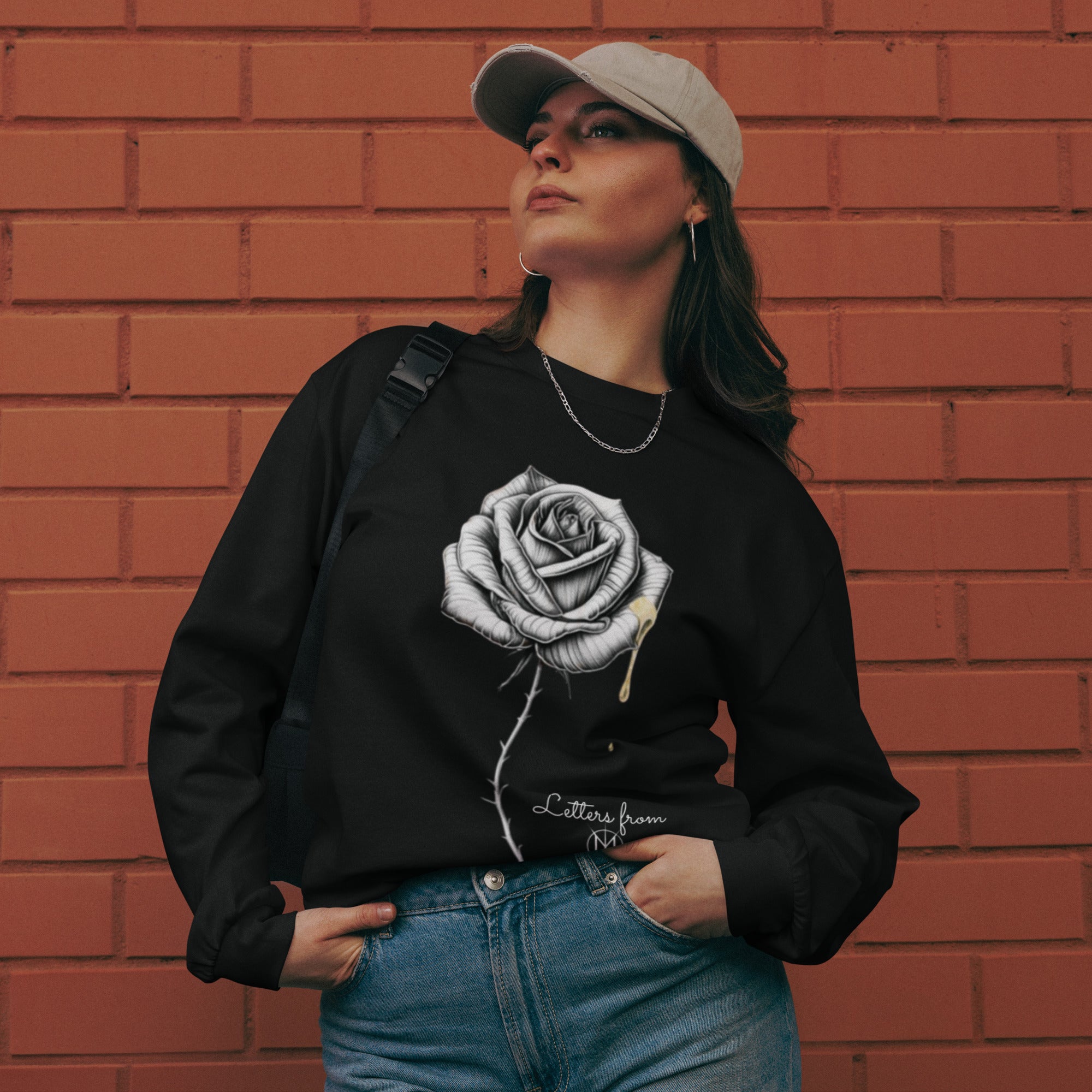 Person wearing a black sweatshirt with a Letters from Mars rose design against a brick wall.