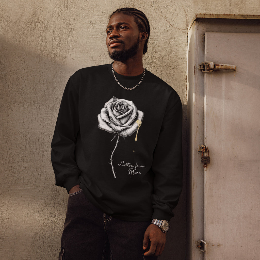 Man wearing a black sweatshirt with a white Letters from Mars rose design, standing against a textured wall.