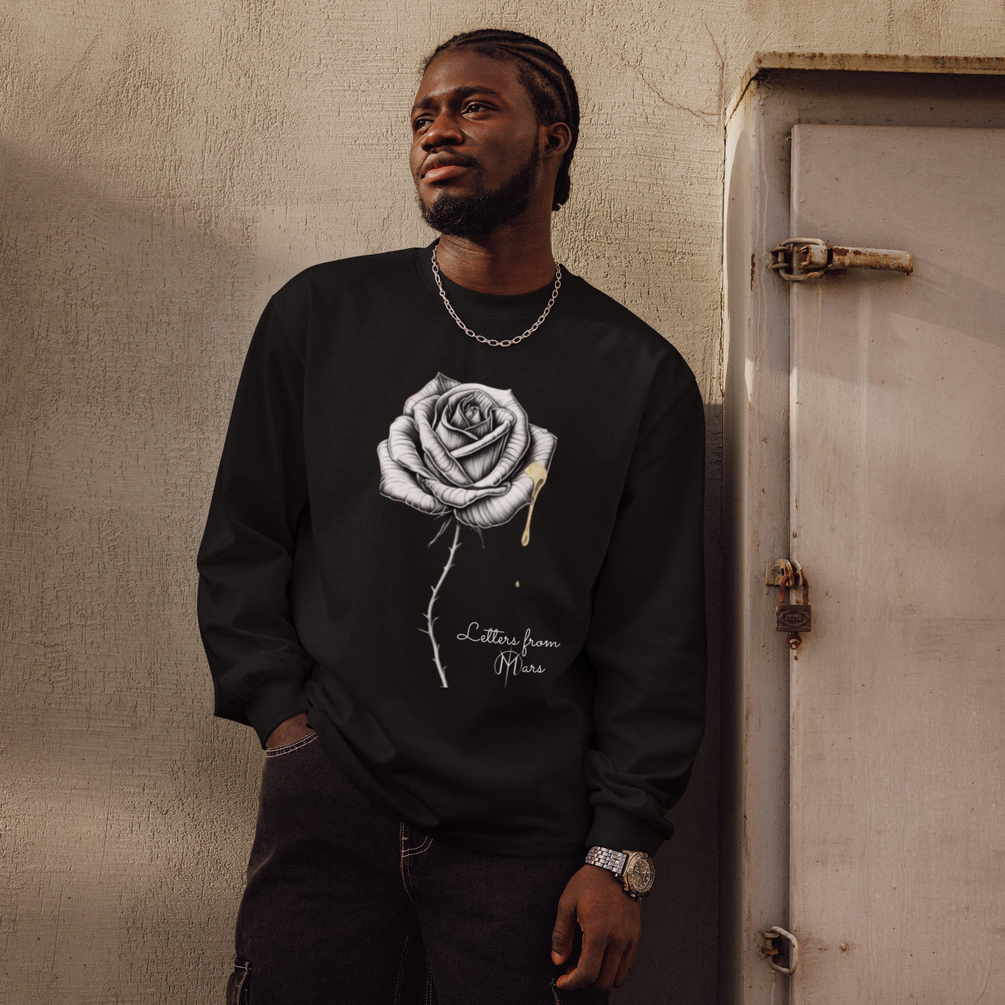 Man wearing a black sweatshirt with a white Letters from Mars rose design, standing against a textured wall.